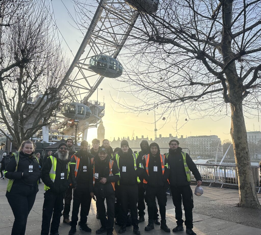 Group photo of the London crew in front of the London Eye, with Big Ben in the background.